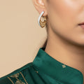 A pair of gold crescent-shaped hoop earrings with silver pavé trim and an openwork filigree center, displayed on a white card against a textured gray background.