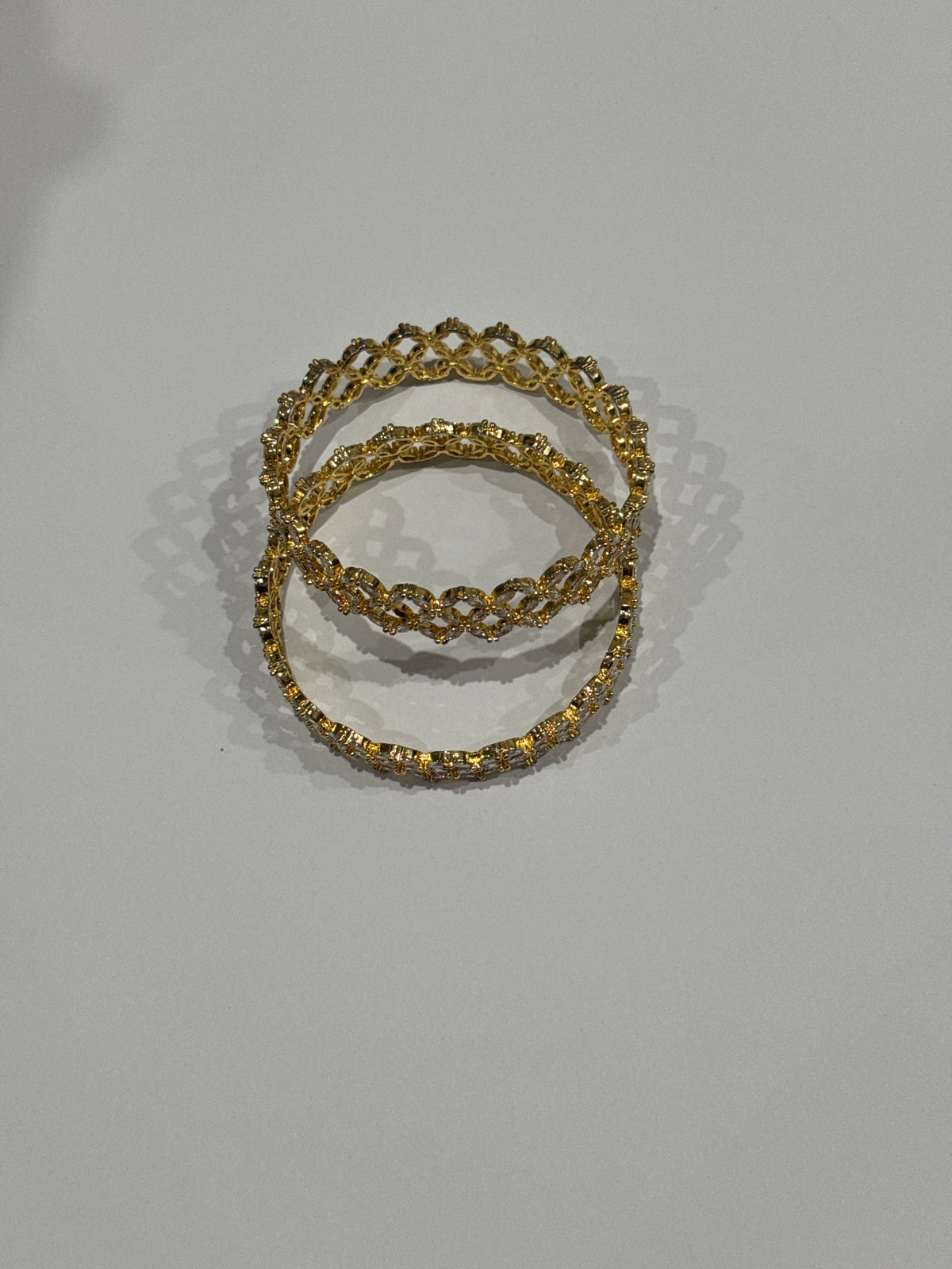 Three gold-toned bangles with intricate floral and geometric filigree patterns, stacked on a light gray background.