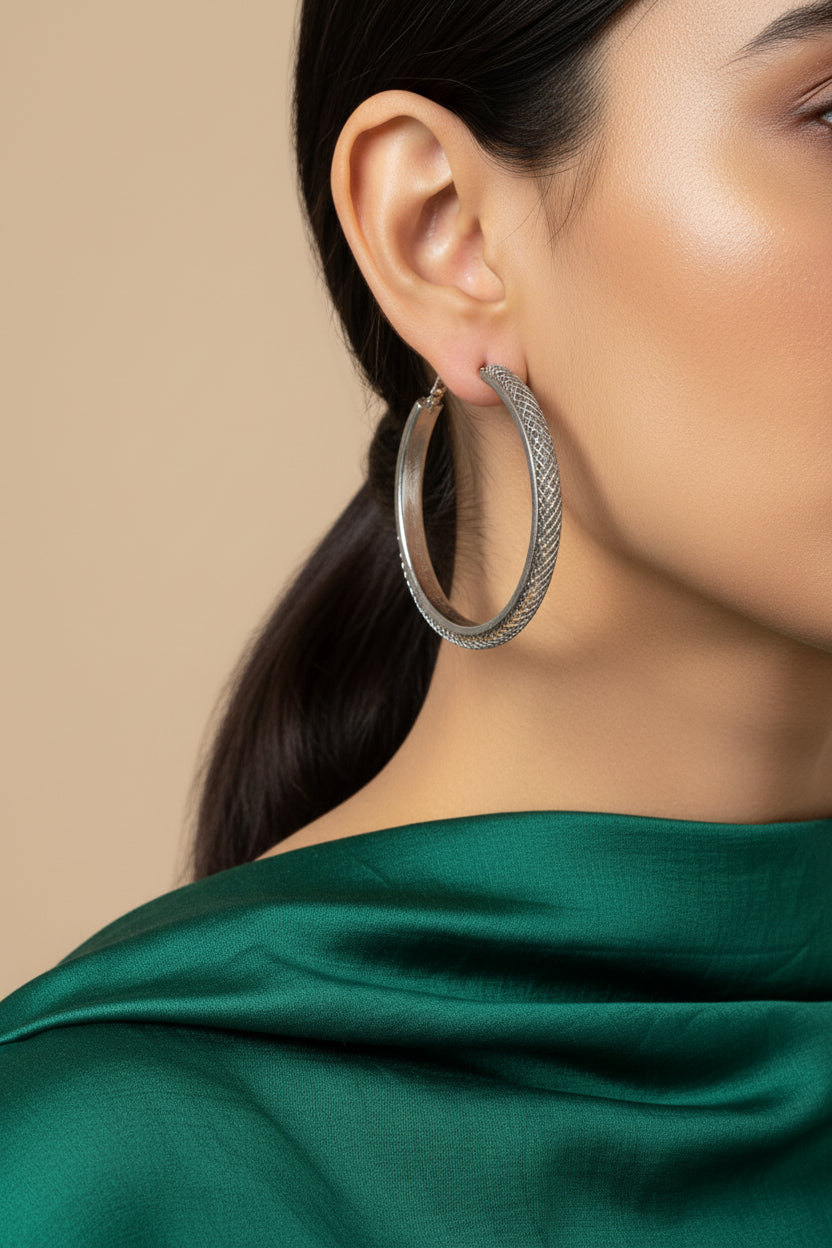 A pair of large silver-tone hoop earrings with a textured, woven mesh pattern on the outer surface, displayed on a plain light gray background.
