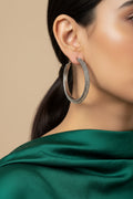 A pair of large silver-tone hoop earrings with a textured, woven mesh pattern on the outer surface, displayed on a plain light gray background.